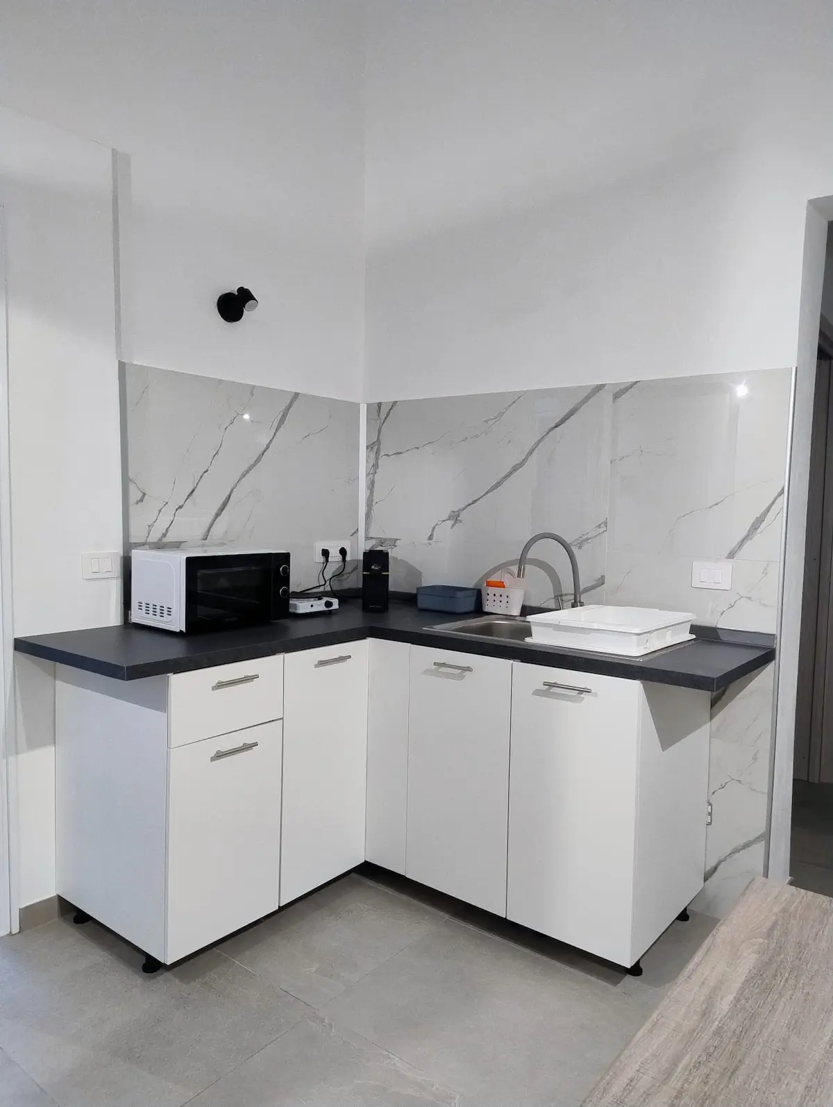 Cucinotto con mobili bianchi, lavello e rivestimento in marmo
